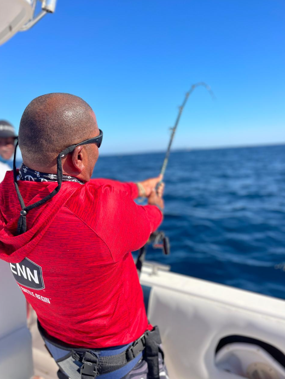 Angler in a red Penn fishing shirt leaning into a bent rod on a charter boat in the deep blue Indian Ocean