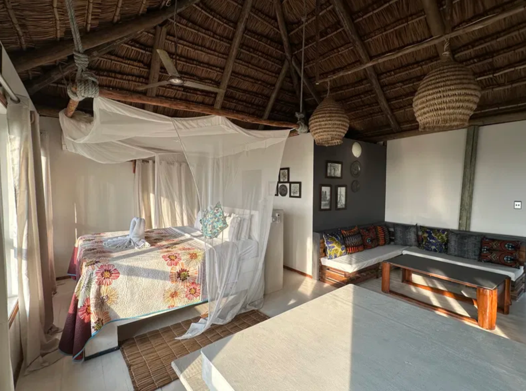 Open bedroom under a thatched roof with lounge seating