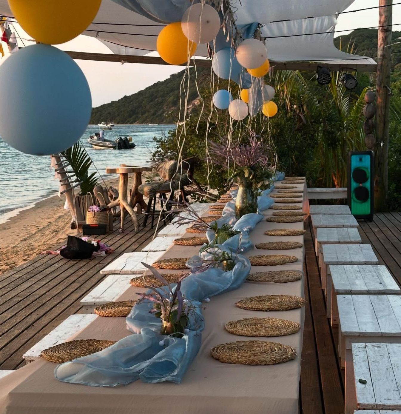 A long beach table decorated with balloons and flowers for a seaside celebration at Bemugi's