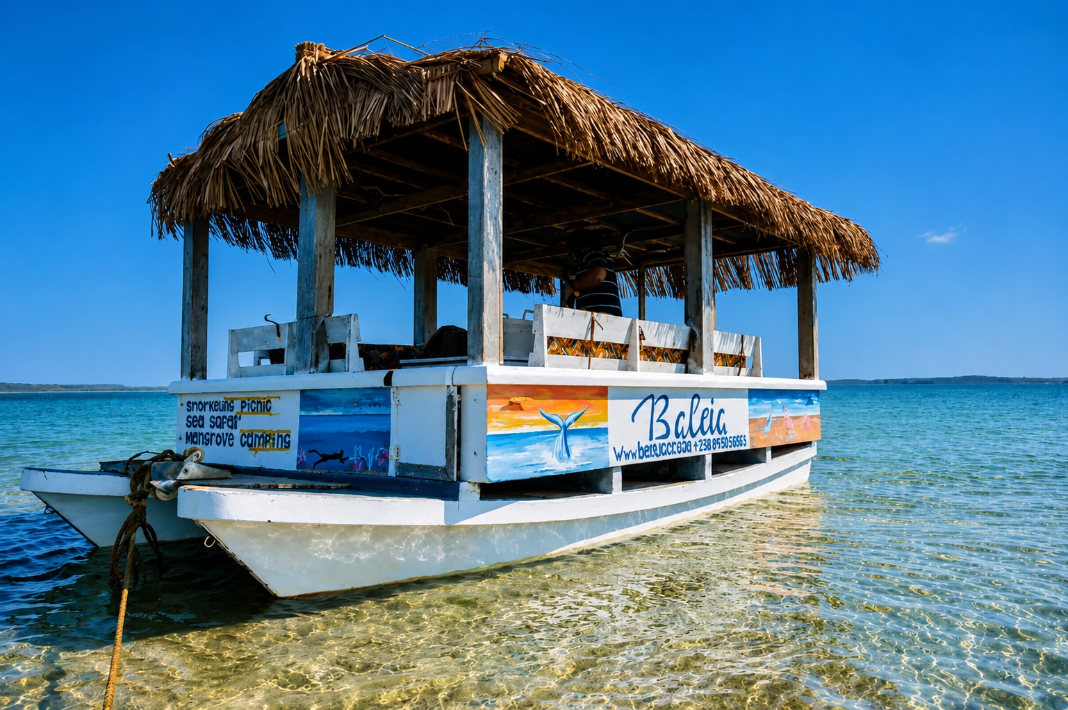 The 'Baleia' boat with thatched roof and colourful side art anchored in shallow turquoise water near Santa Maria