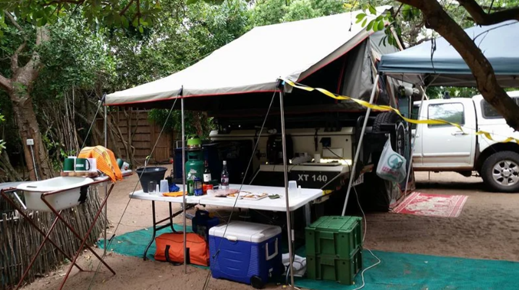 Camp kitchen with awning, table and cooler boxes at a shaded site