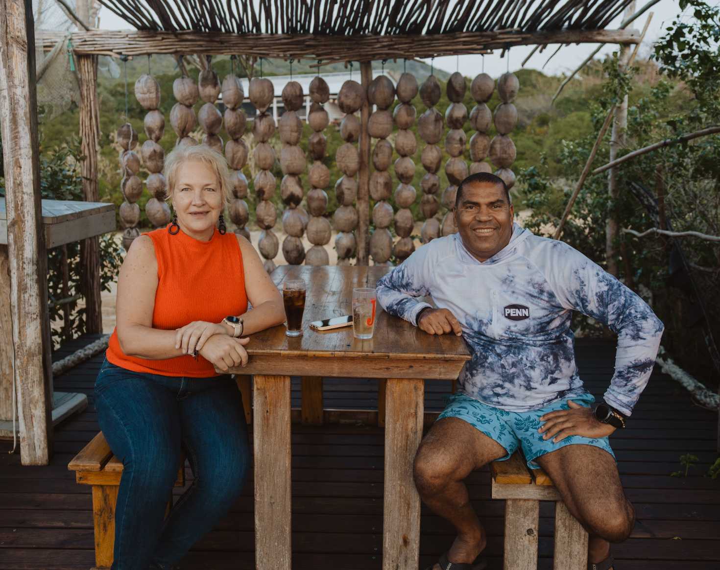 Two people enjoying drinks at the Bemugi's deck with coconuts hanging behind them