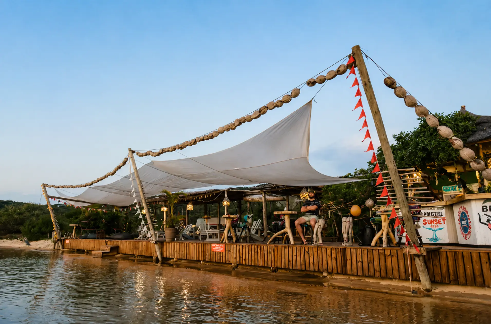 Bemugi's Sunset Deck beach bar over the water with sail shade and flags