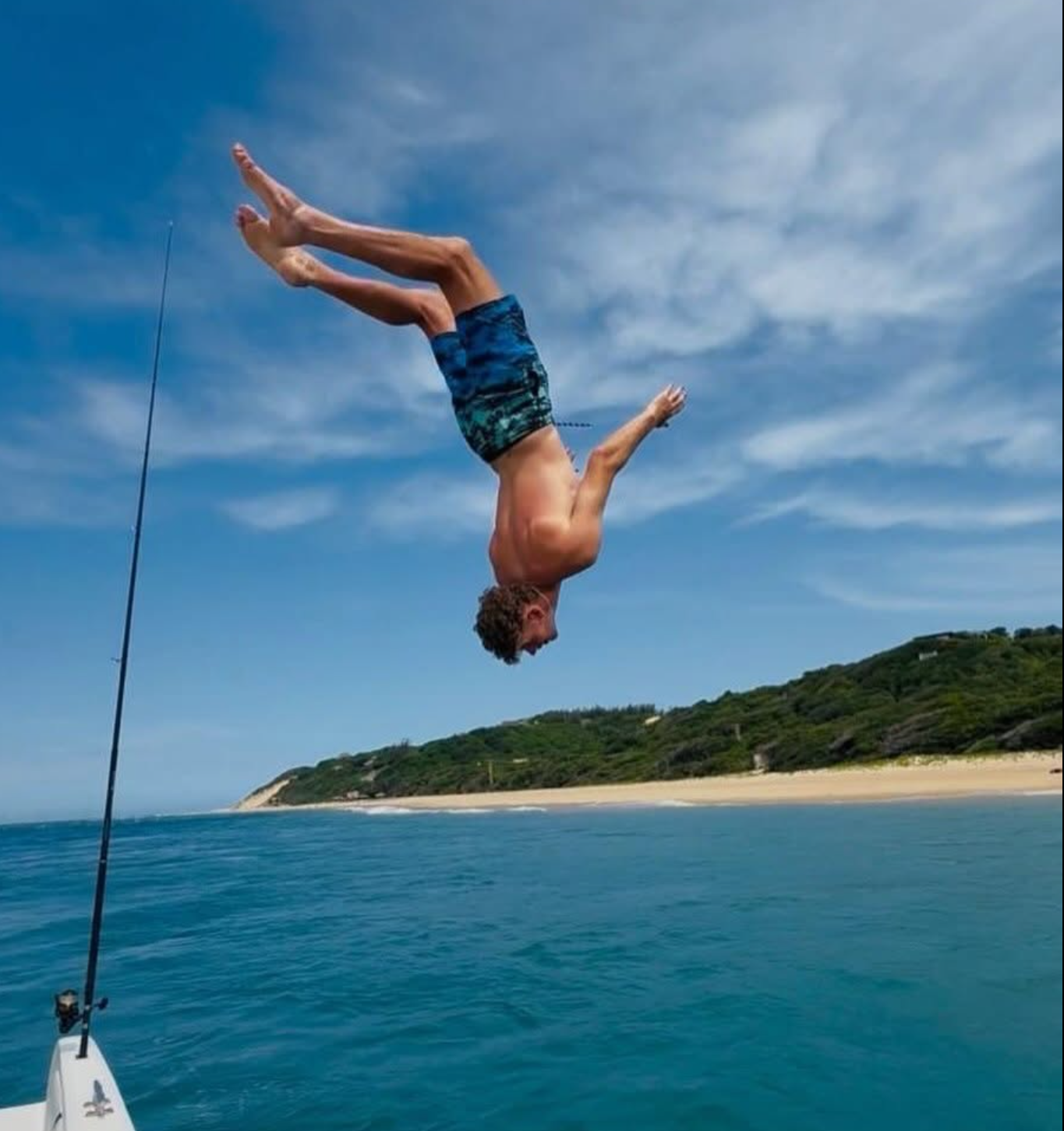 A guest backflipping off a boat into the clear blue water near Bemugi's